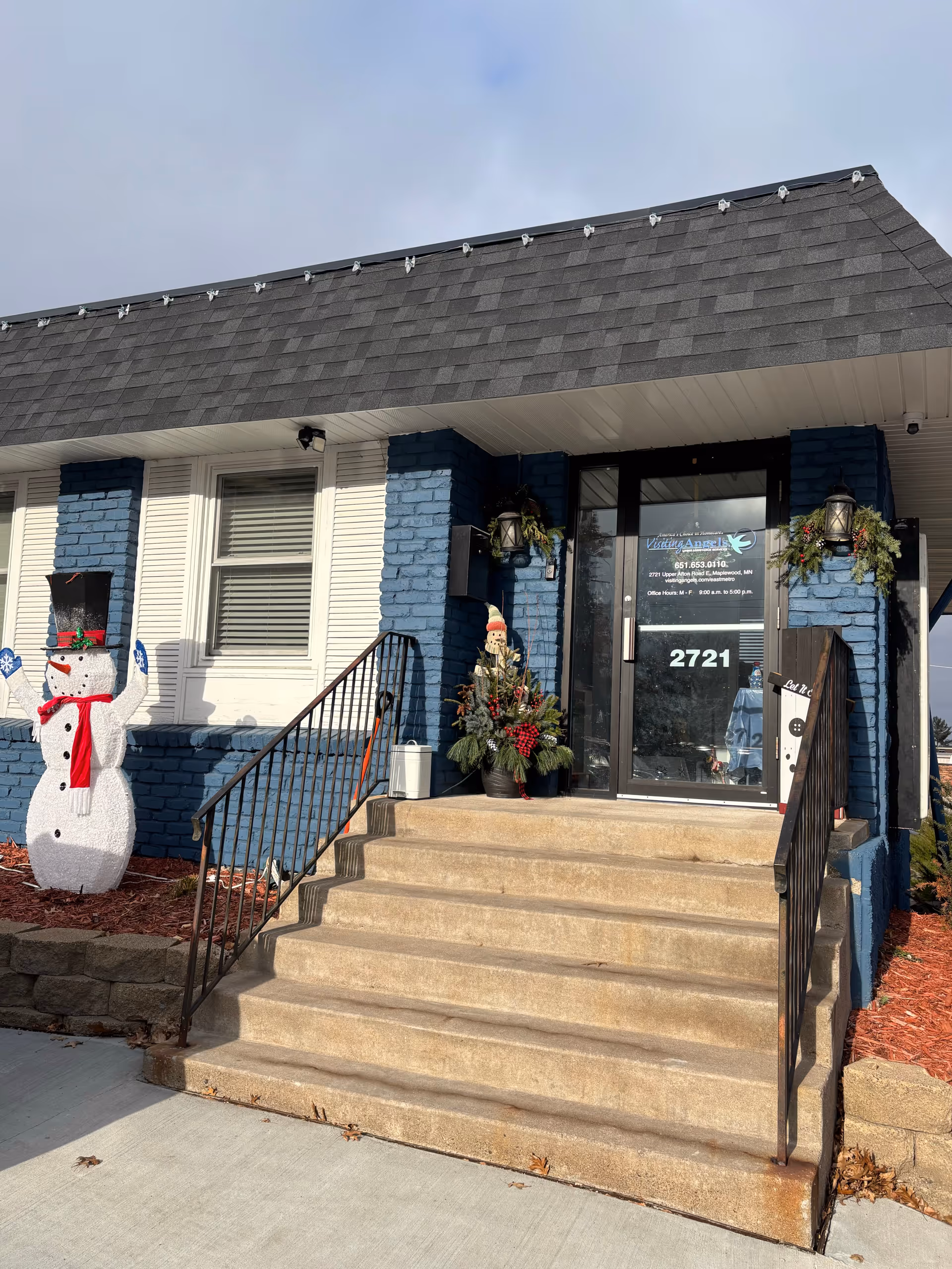 Exterior entrance of Visiting Angels Senior Home Care with blue brick facade, stairs, and holiday decorations.