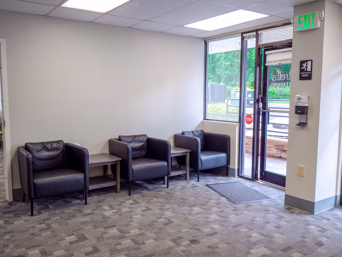 Lobby seating area with black leather chairs, small tables, and a glass exit door.