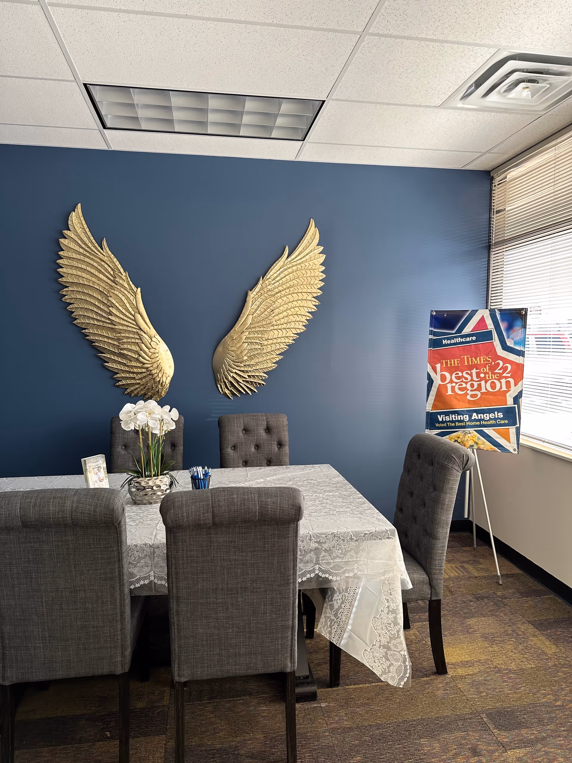 Dining room with blue wall, gold wing sculptures, lace tablecloth, and gray chairs.