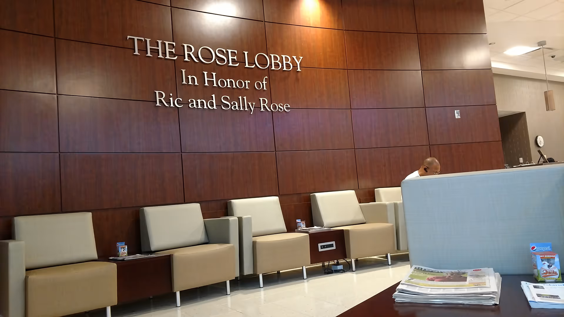 Wood-paneled lobby with beige seating and a reception desk; sign reads The Rose Lobby.