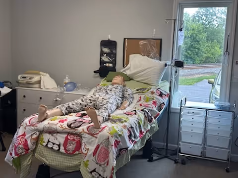 A patient rests in a floral-patterned bed in a small private hospital room.