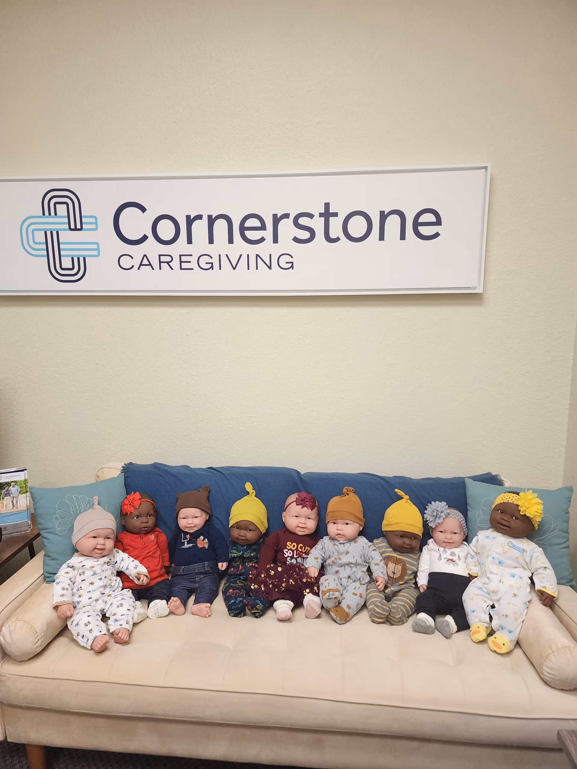 Interior lounge area with Cornerstone Caregiving sign and a row of baby dolls on a couch.