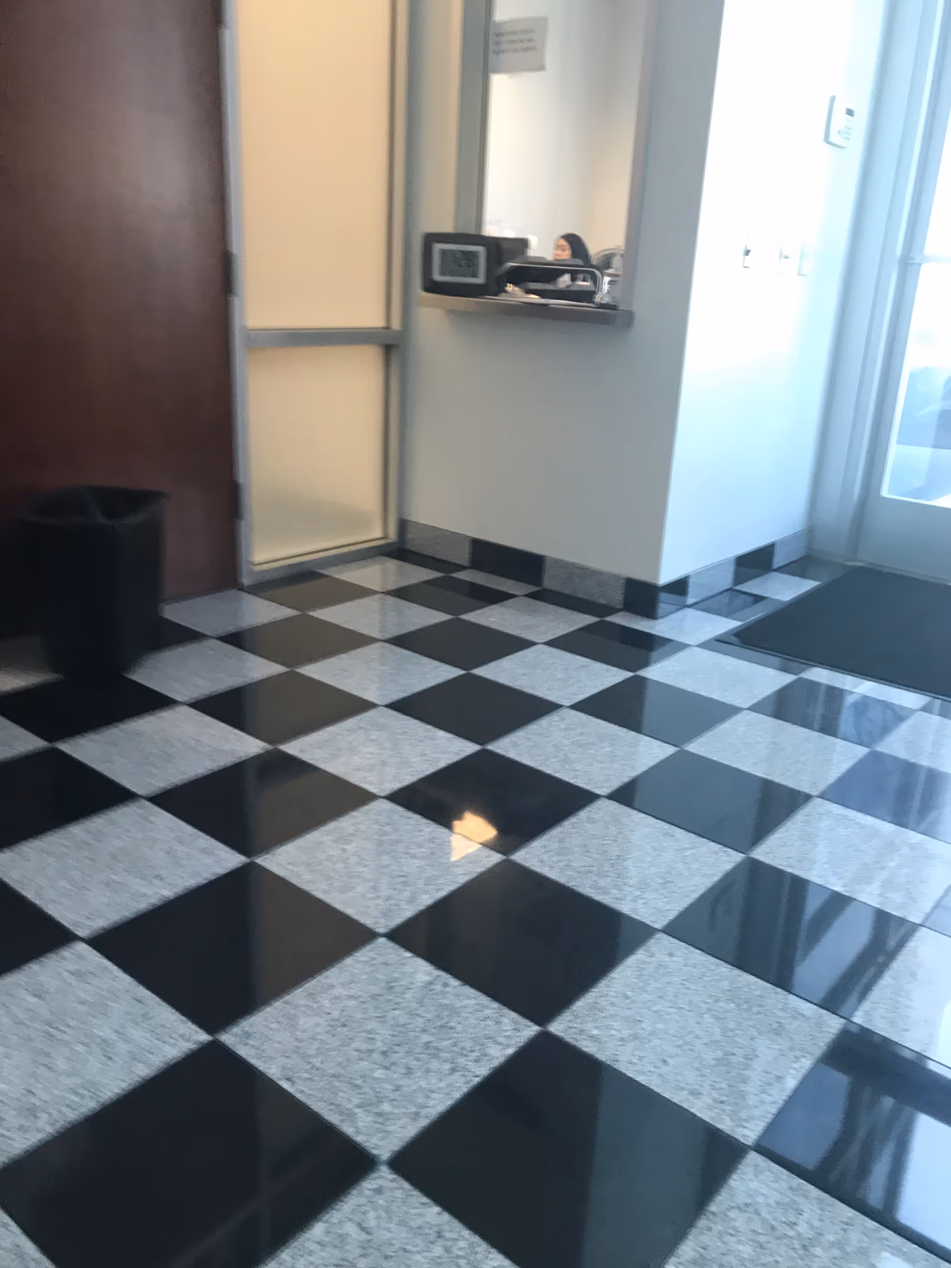 Checkerboard black and gray tile lobby floor with a service window and a person behind desk.