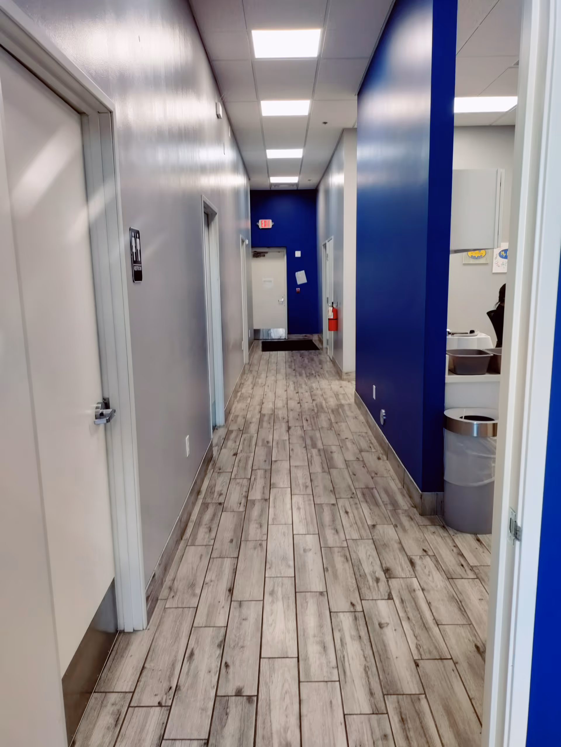 A clean indoor hallway with blue walls, doors, and overhead fluorescent lights.