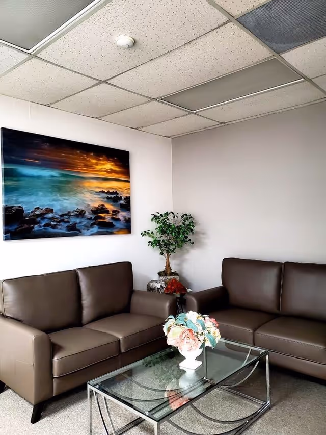 L-shaped brown leather sofas, glass coffee table, and a potted plant in a quiet waiting lounge.