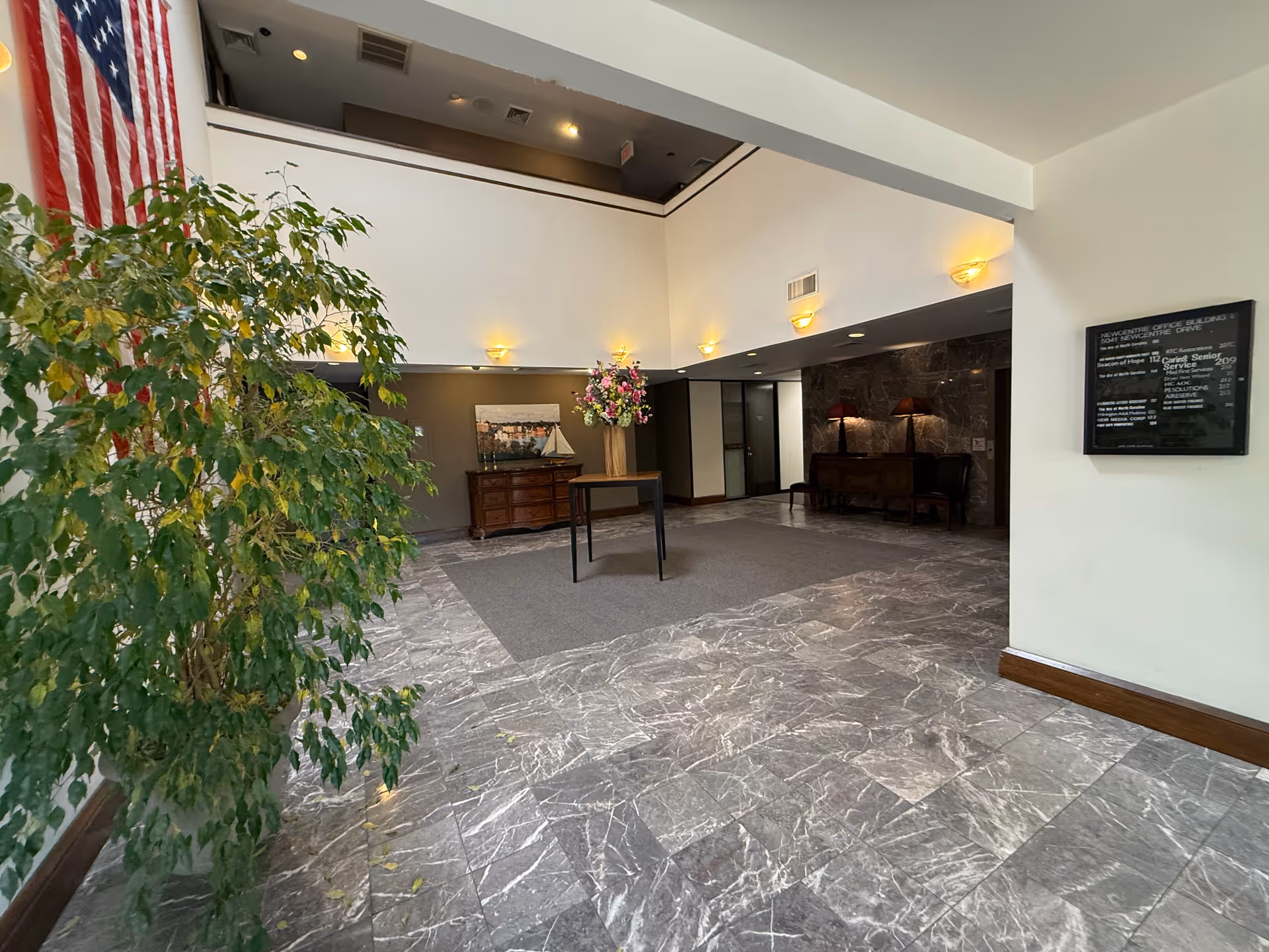 Interior lobby with marble flooring, large plant, American flag, and reception area.