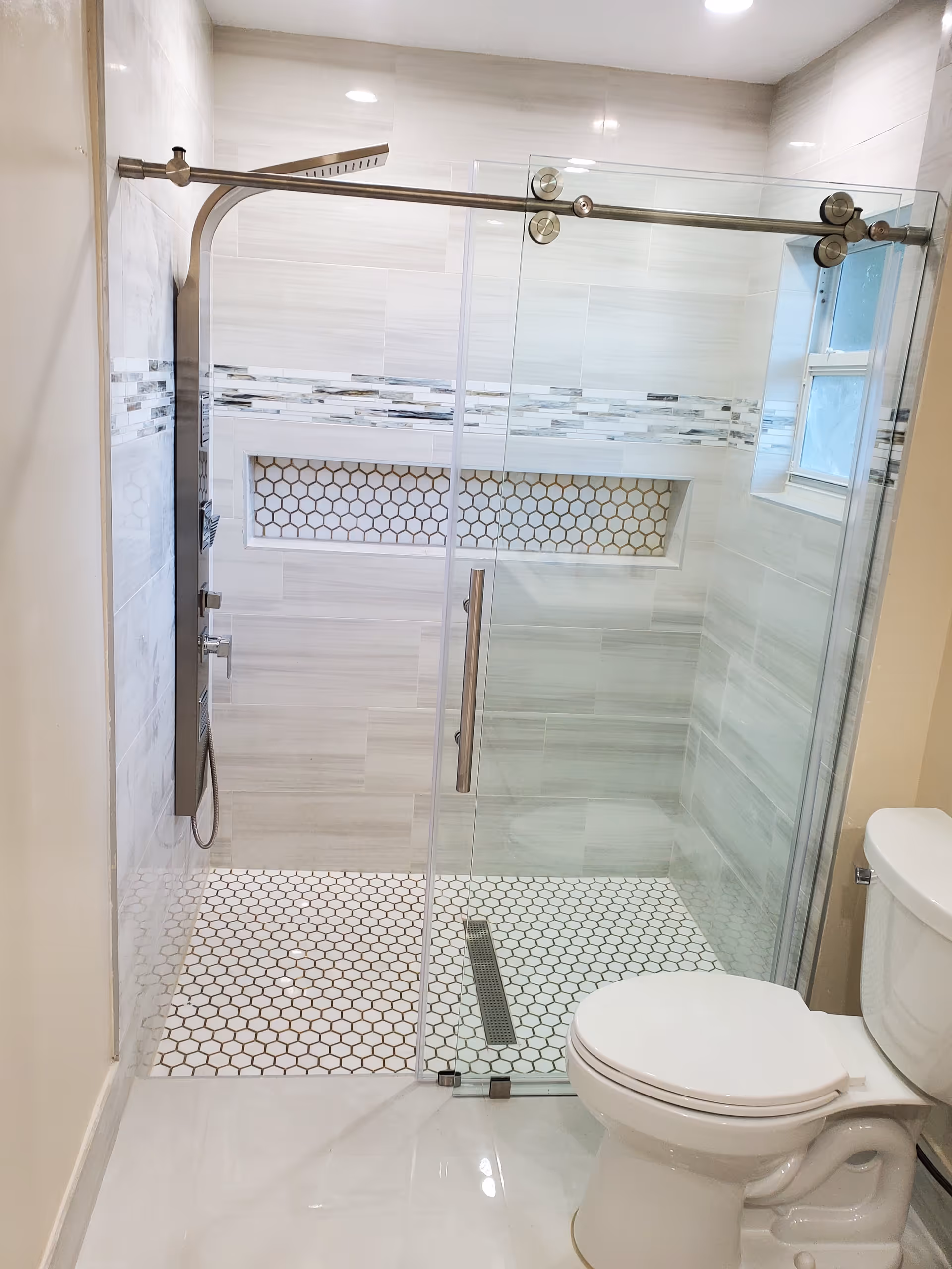 Modern bathroom with glass shower enclosure and white hex-tile accents.