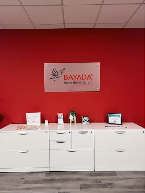Reception area with white cabinets and BAYADA sign on red wall.