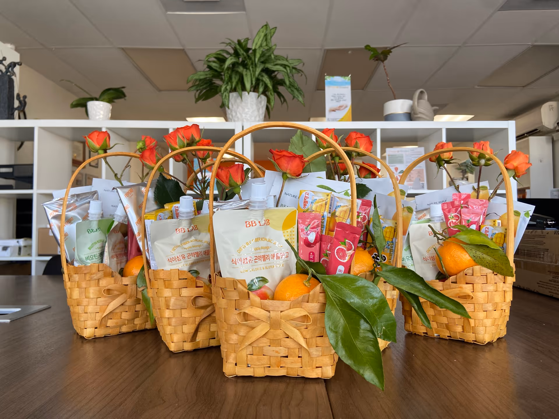 Four wicker baskets filled with snacks and oranges sit on a wooden table inside a facility.
