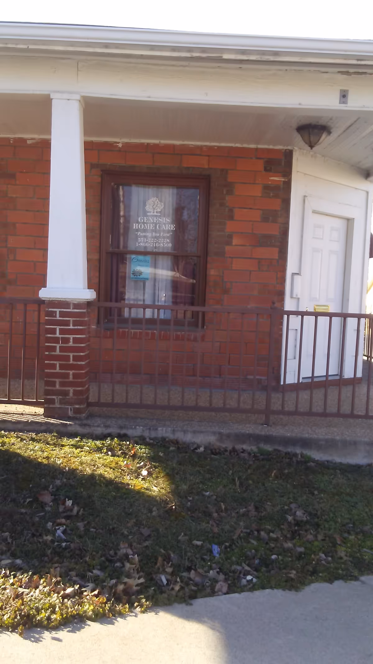 Brick building front with white pillars, railing, door, and Genesis Home Care window sign.