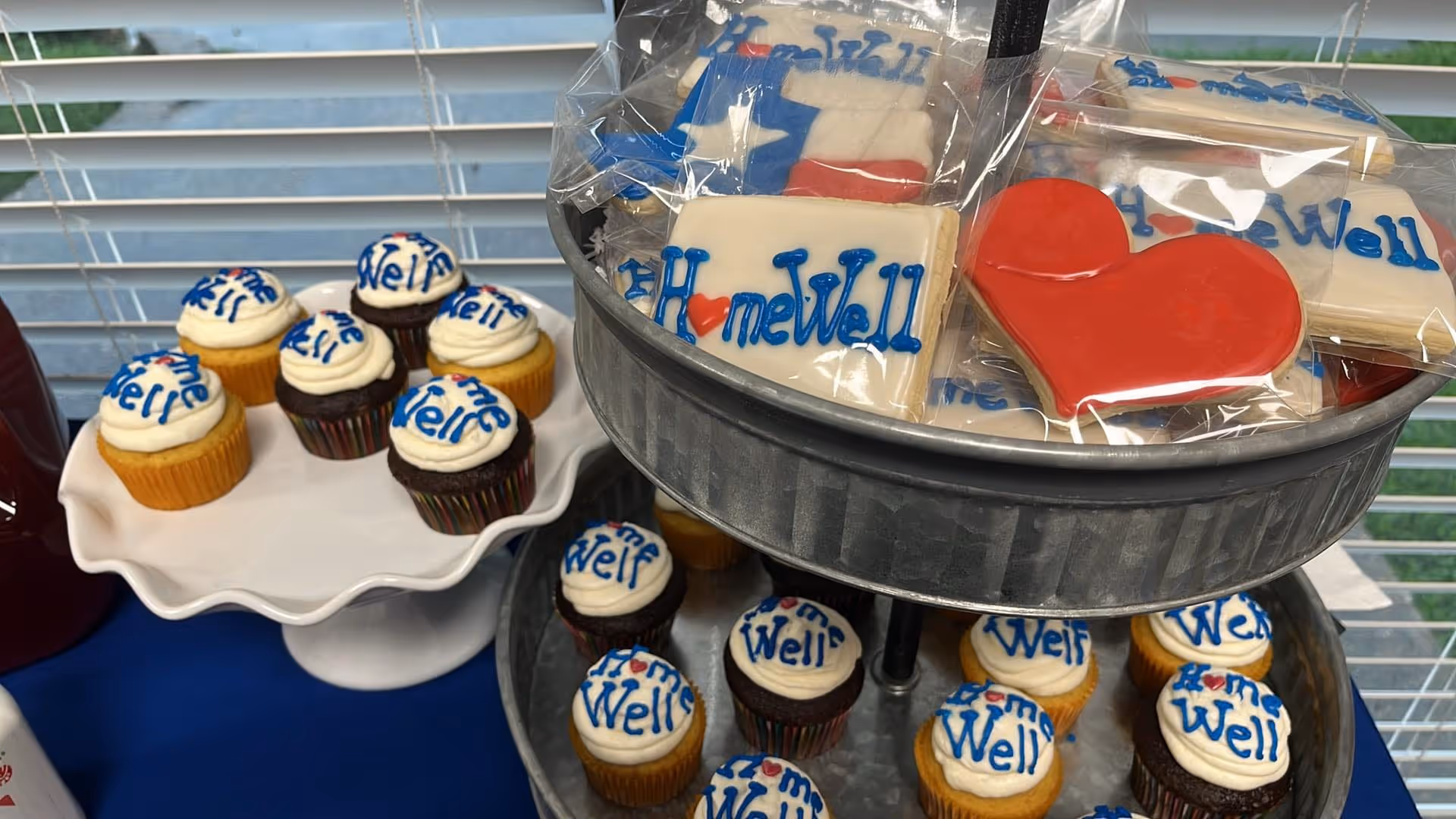 Tiered metal display holds HomeWell-branded cupcakes and cookies.