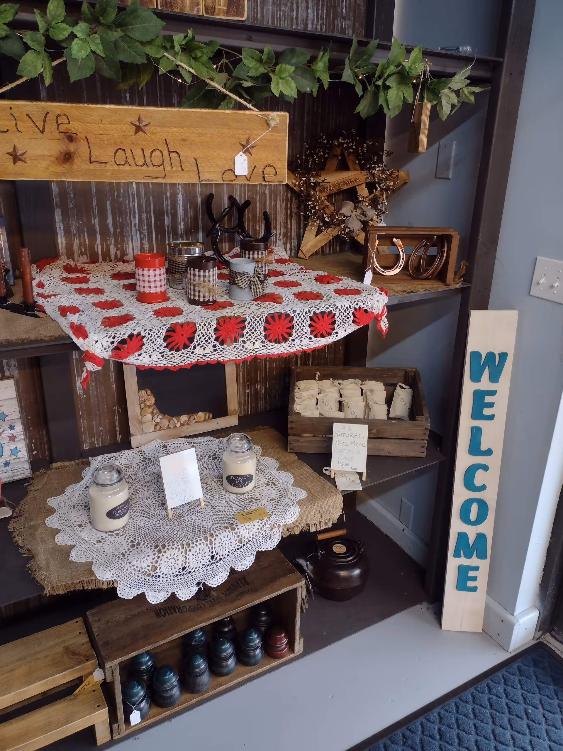 Rustic interior display with a welcome sign, jars, candles, and crocheted doilies.