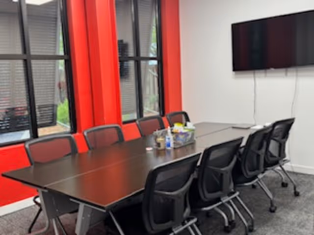 A long conference table with chairs in a bright meeting room with red accents.