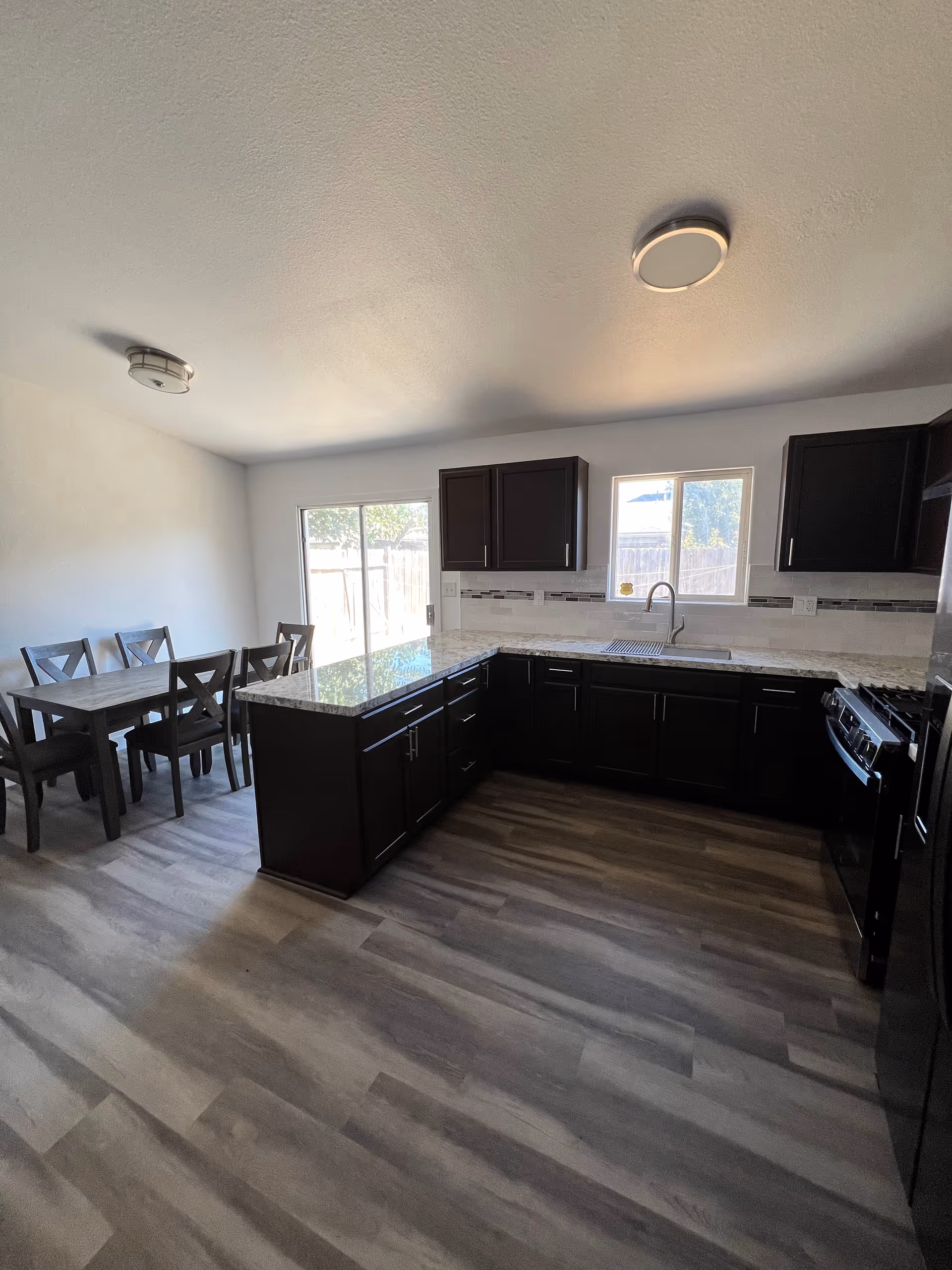Modern L-shaped kitchen with dark cabinets, granite countertops, an island, and a dining table.