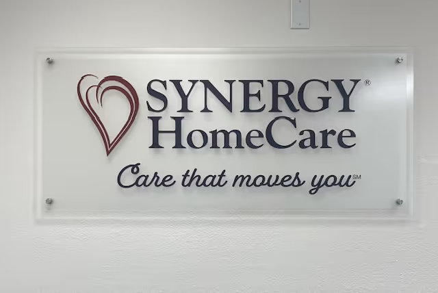 Sign reads SYNERGY HomeCare with heart logo and motto on wall.
