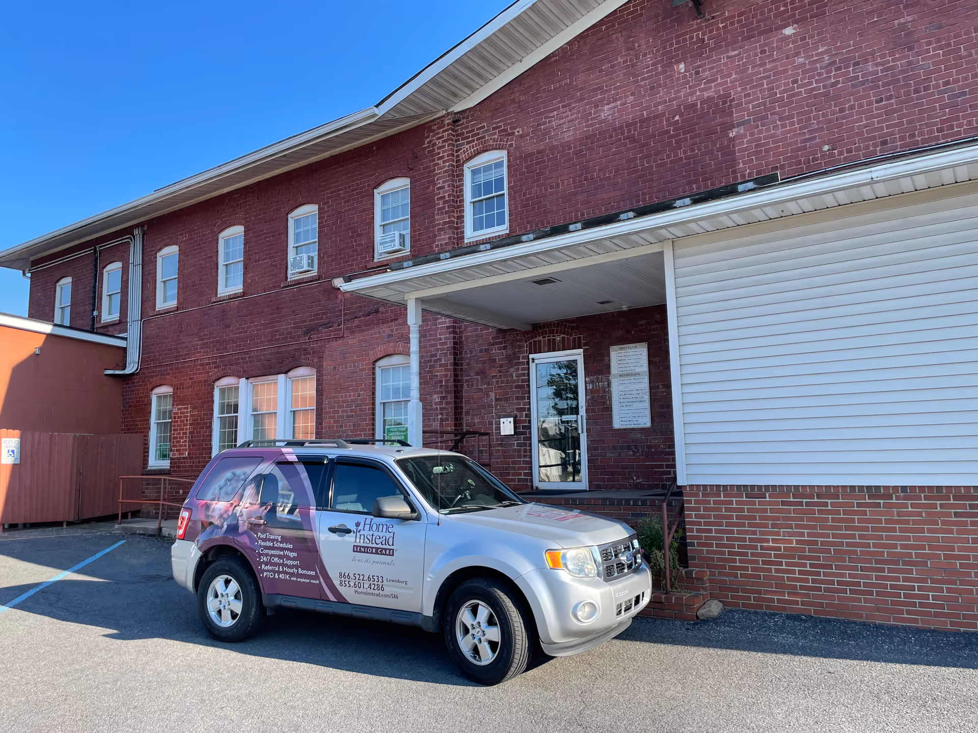 A Home Instead vehicle parked in front of a red brick senior care facility entrance.