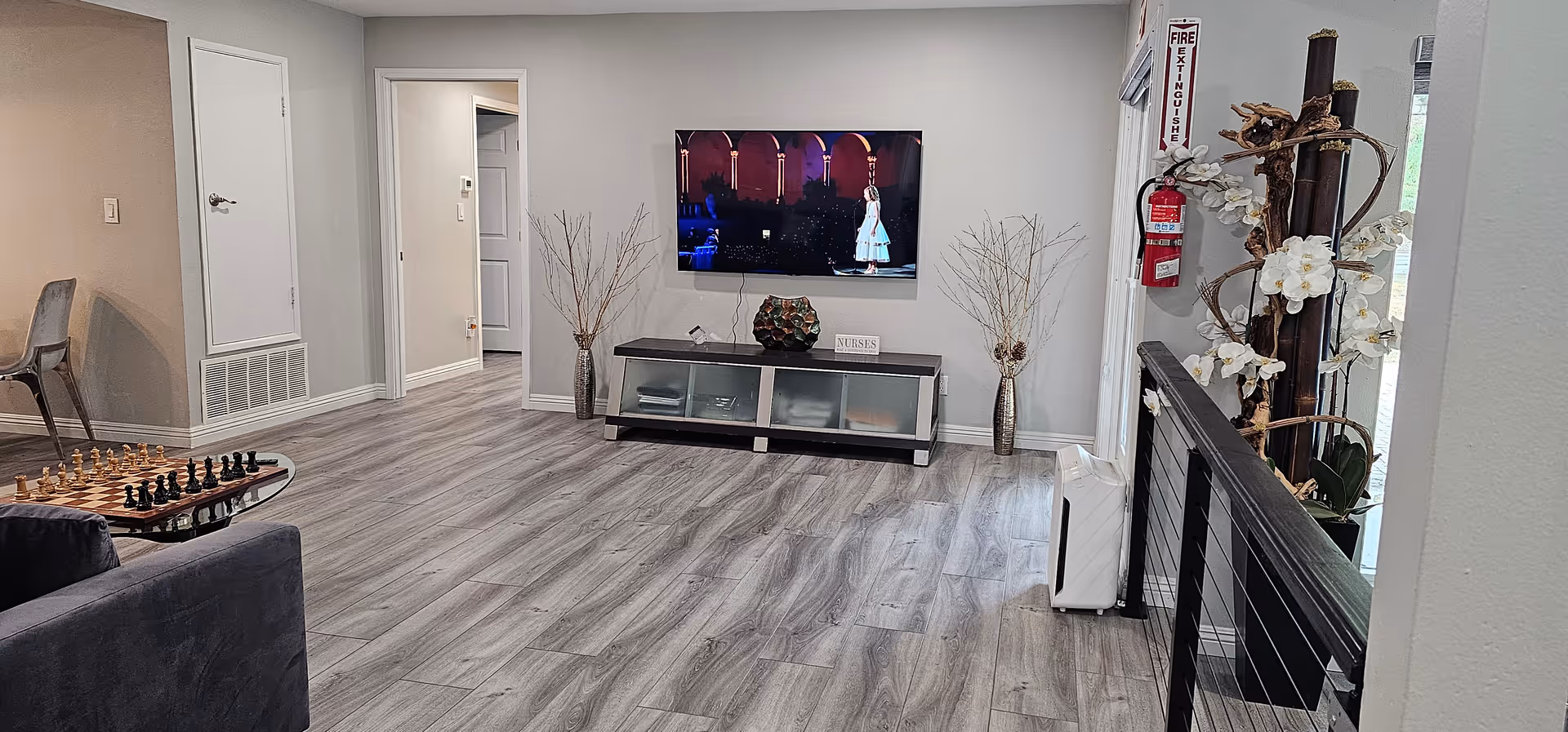 Modern senior living common area with wall-mounted TV, console, decorative vases, and seating.