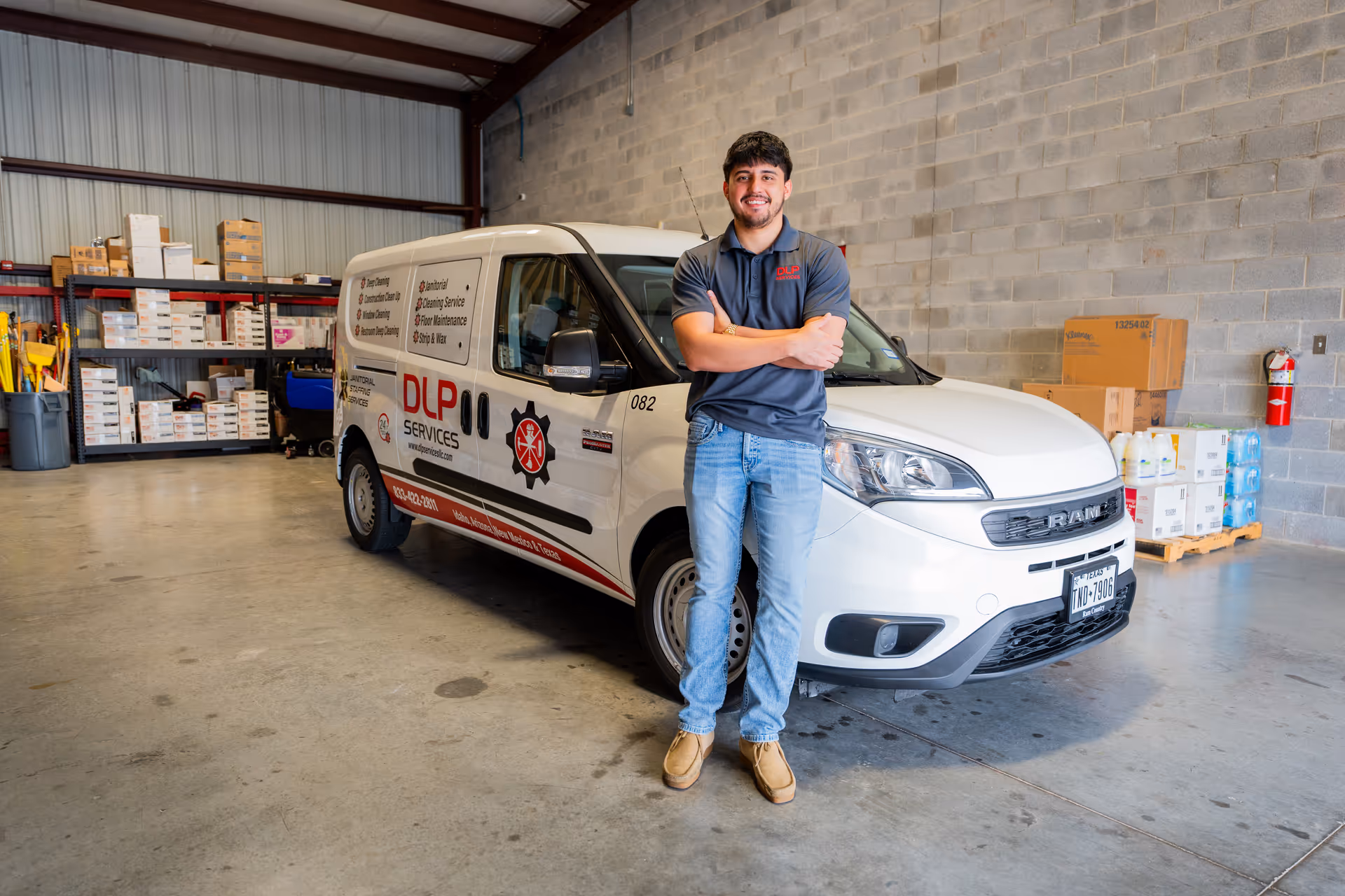 Man stands with arms crossed beside a DLP Services van inside a warehouse.