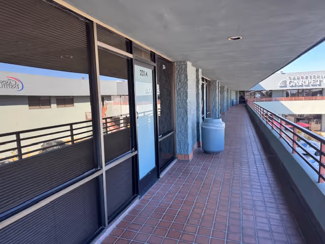 Exterior balcony walkway of a senior living facility with glass doors, tiled floor, and railing.
