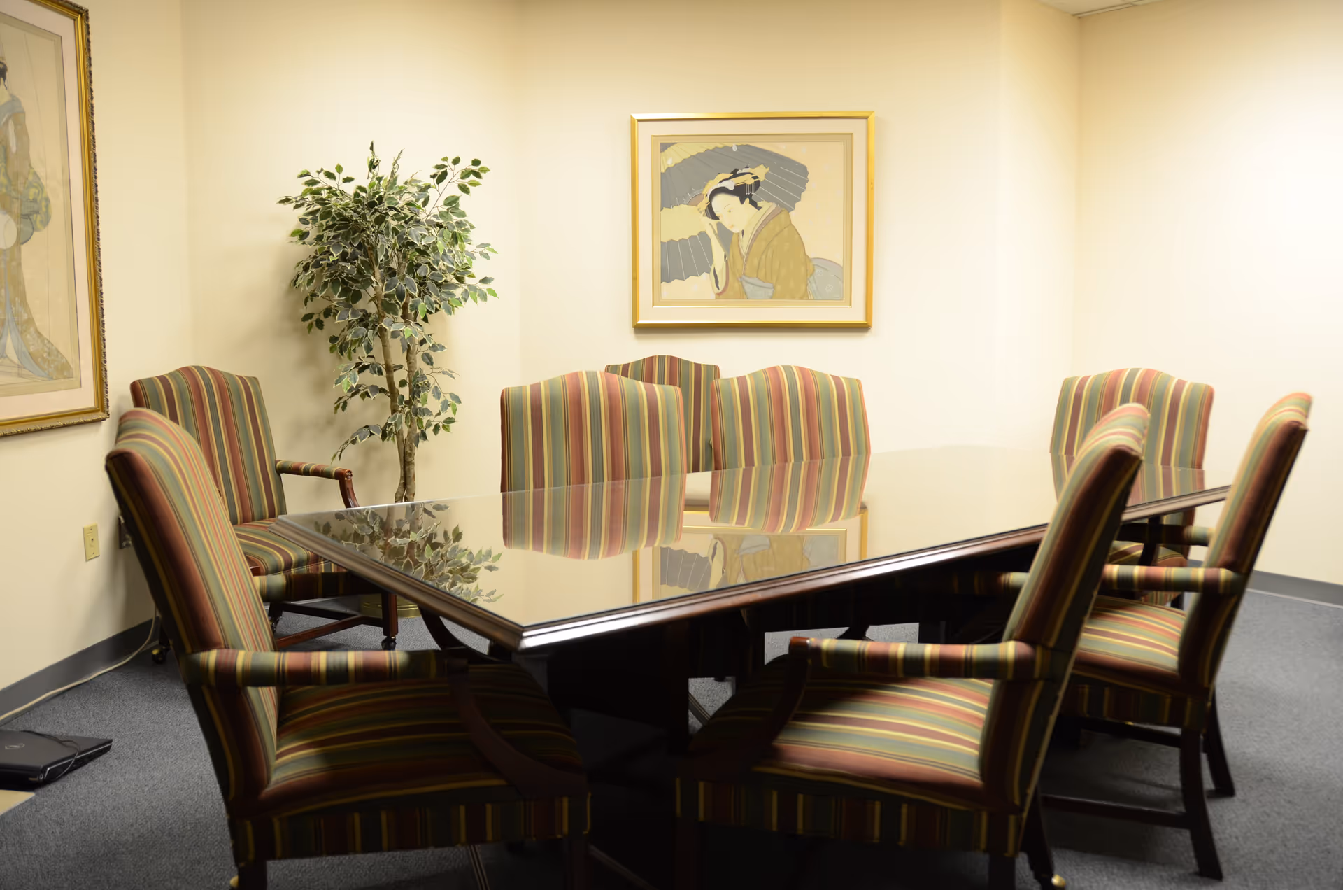 Glass-top conference table surrounded by striped chairs in a small, art-adorned meeting room.