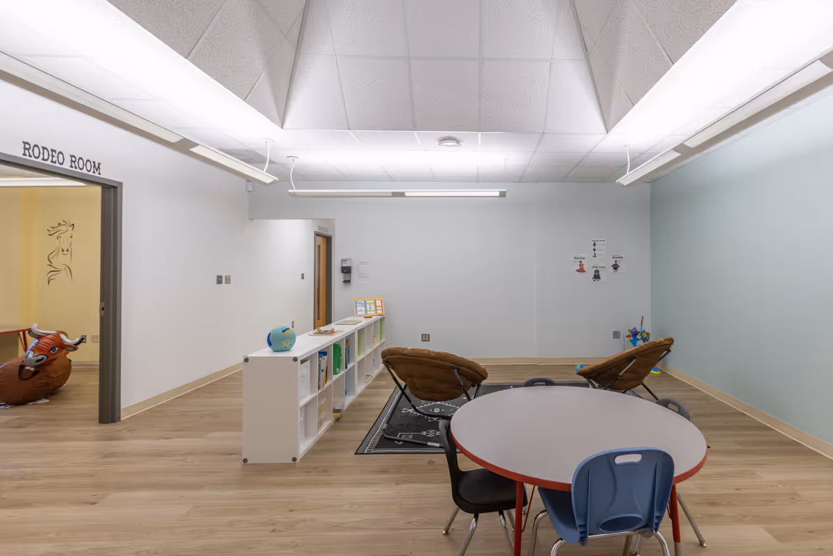 Bright interior activity room with round table, chairs, and shelves with toys in a senior facility.