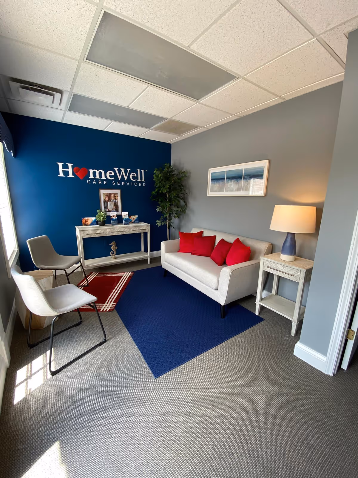 Cozy reception lounge with blue accent wall, sofa, chairs, and HomeWell logo.