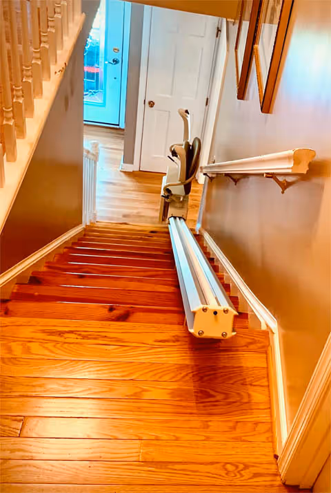 Indoor staircase with a wall-mounted chairlift along wooden steps.