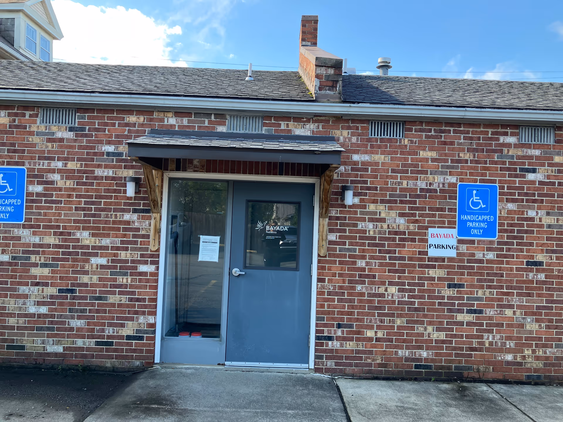 Brick building entrance with blue door, Bayada logo, and handicapped parking signs.