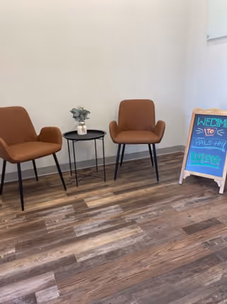 Two brown armchairs flank a small round table with a plant in a lobby.