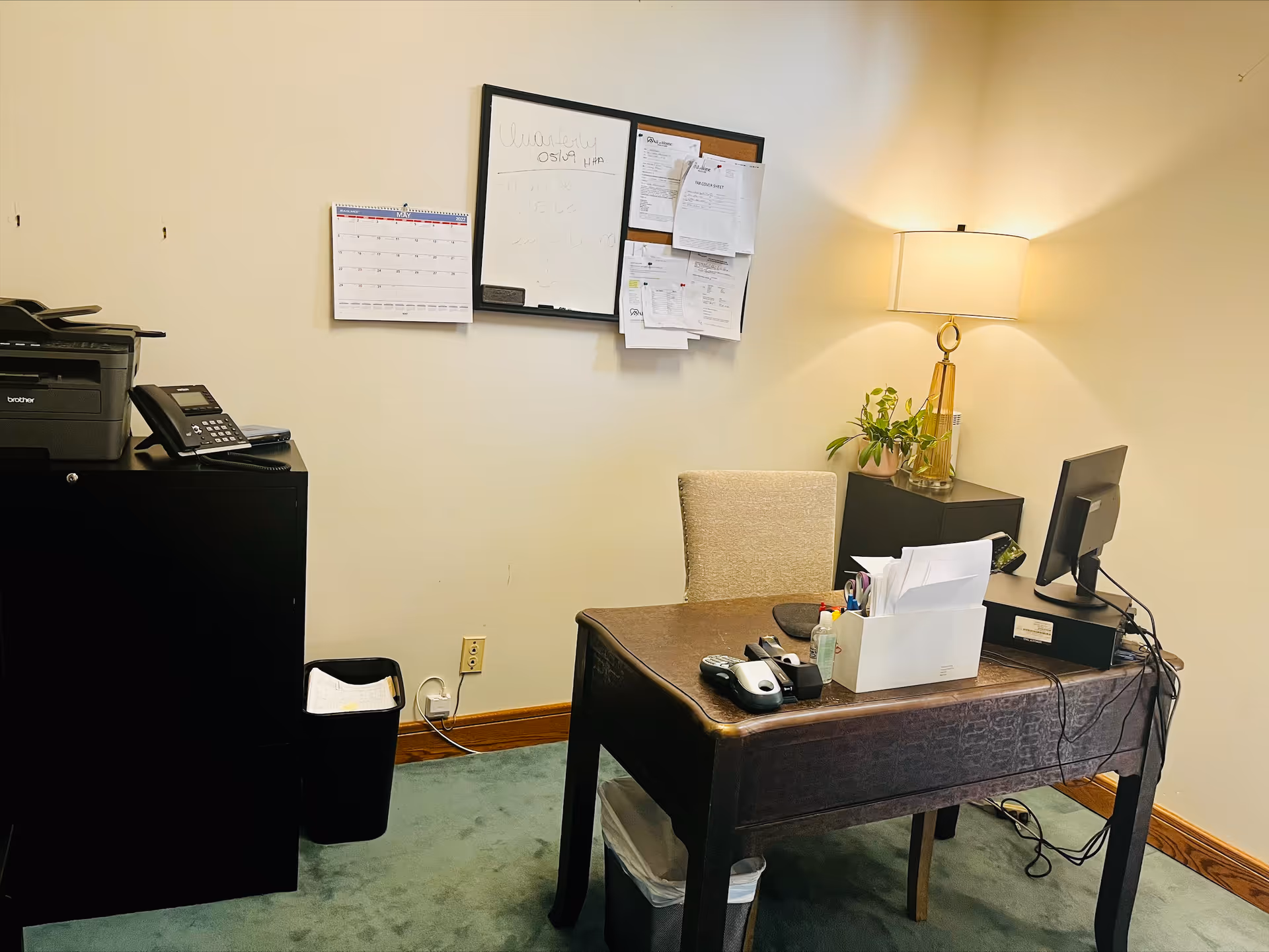 Office workspace with a desk, computer, printer, lamp, plant, and paperwork.