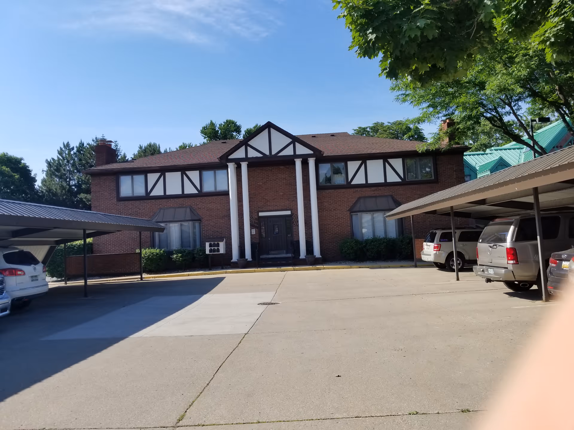 Brick senior living facility with Tudor-style facade and parked cars under carports.