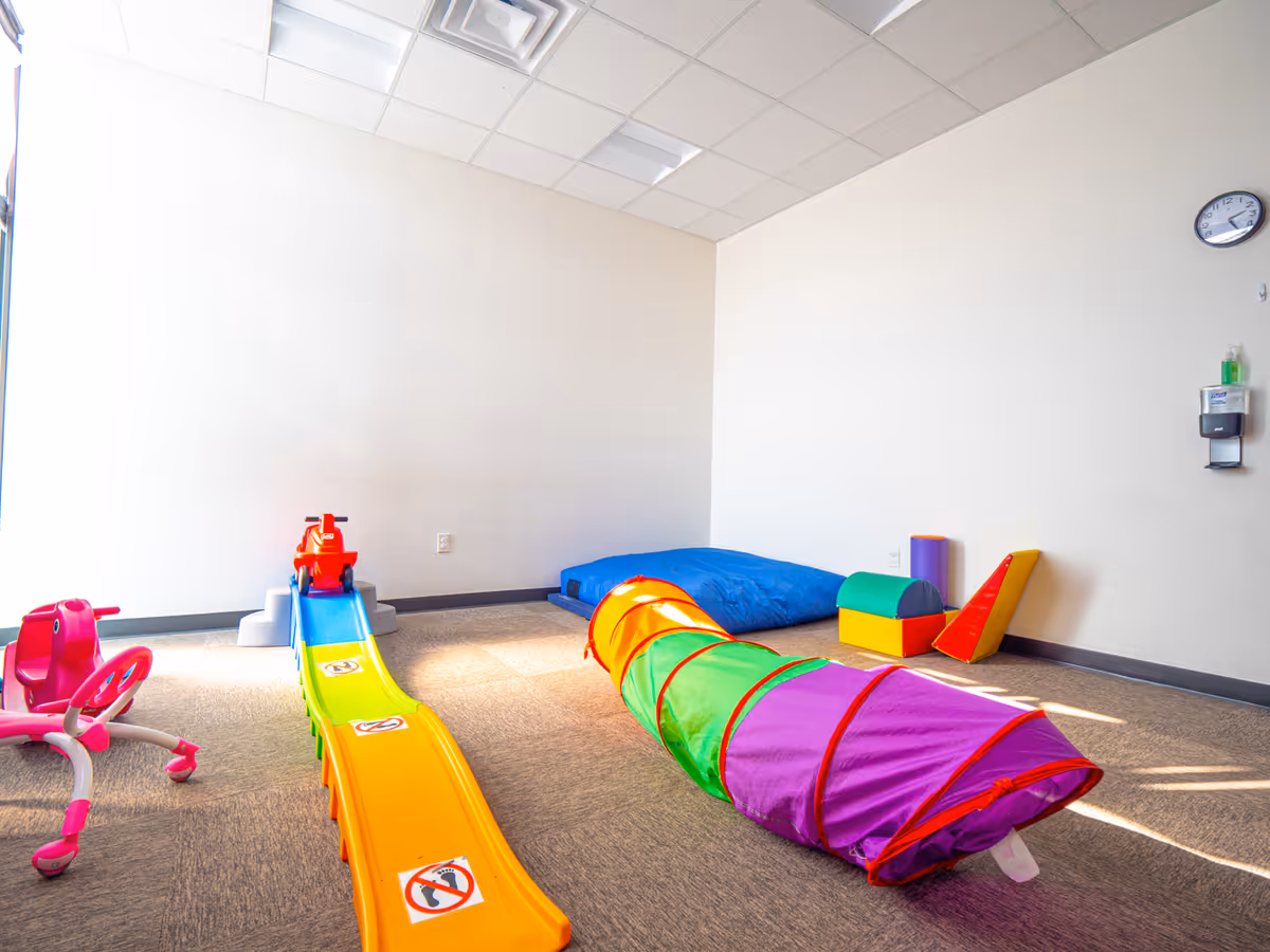 Bright room filled with colorful play equipment and soft foam tunnels.