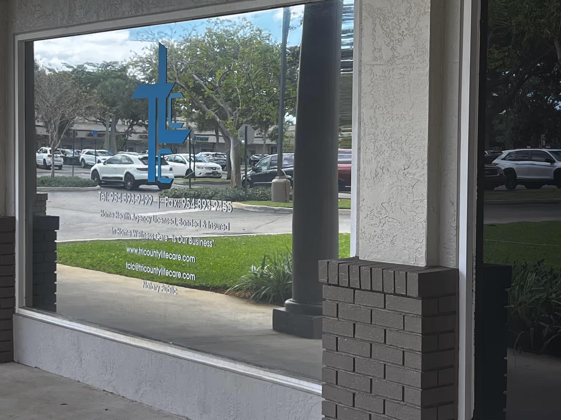 View through a glass storefront window showing Tri-County Life Care signage and parked cars.