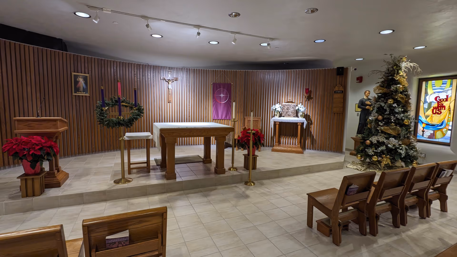Interior chapel area with altar, crucifix, wreaths, poinsettias, and a Christmas tree.