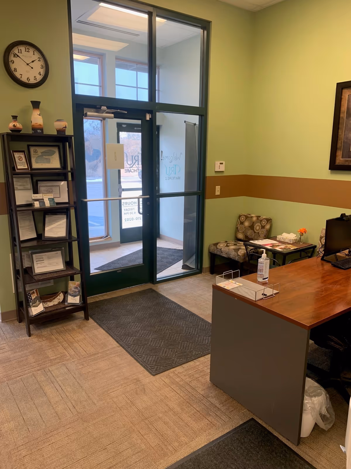 Lobby area with a wooden desk, seating, brochure rack, clock, and glass entrance door.