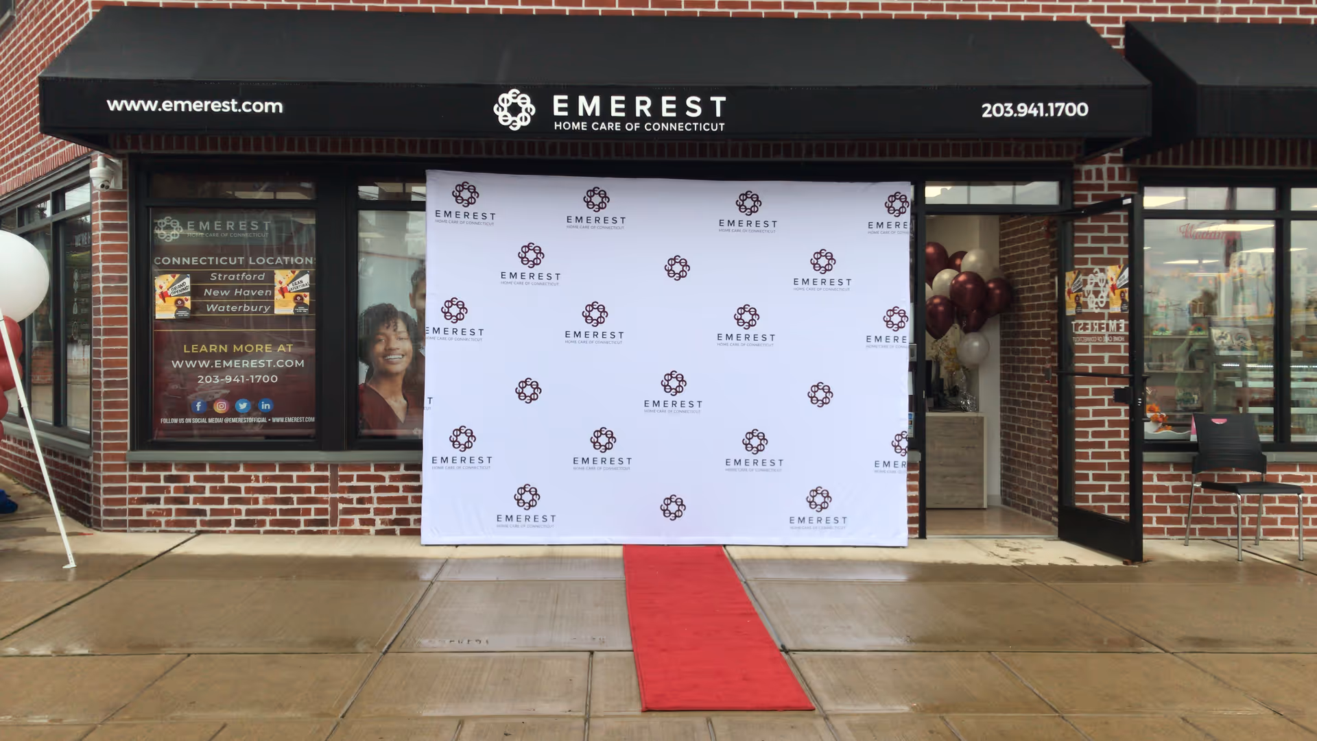 Brick storefront with black canopy, red carpet, and white branded backdrop at the entrance.