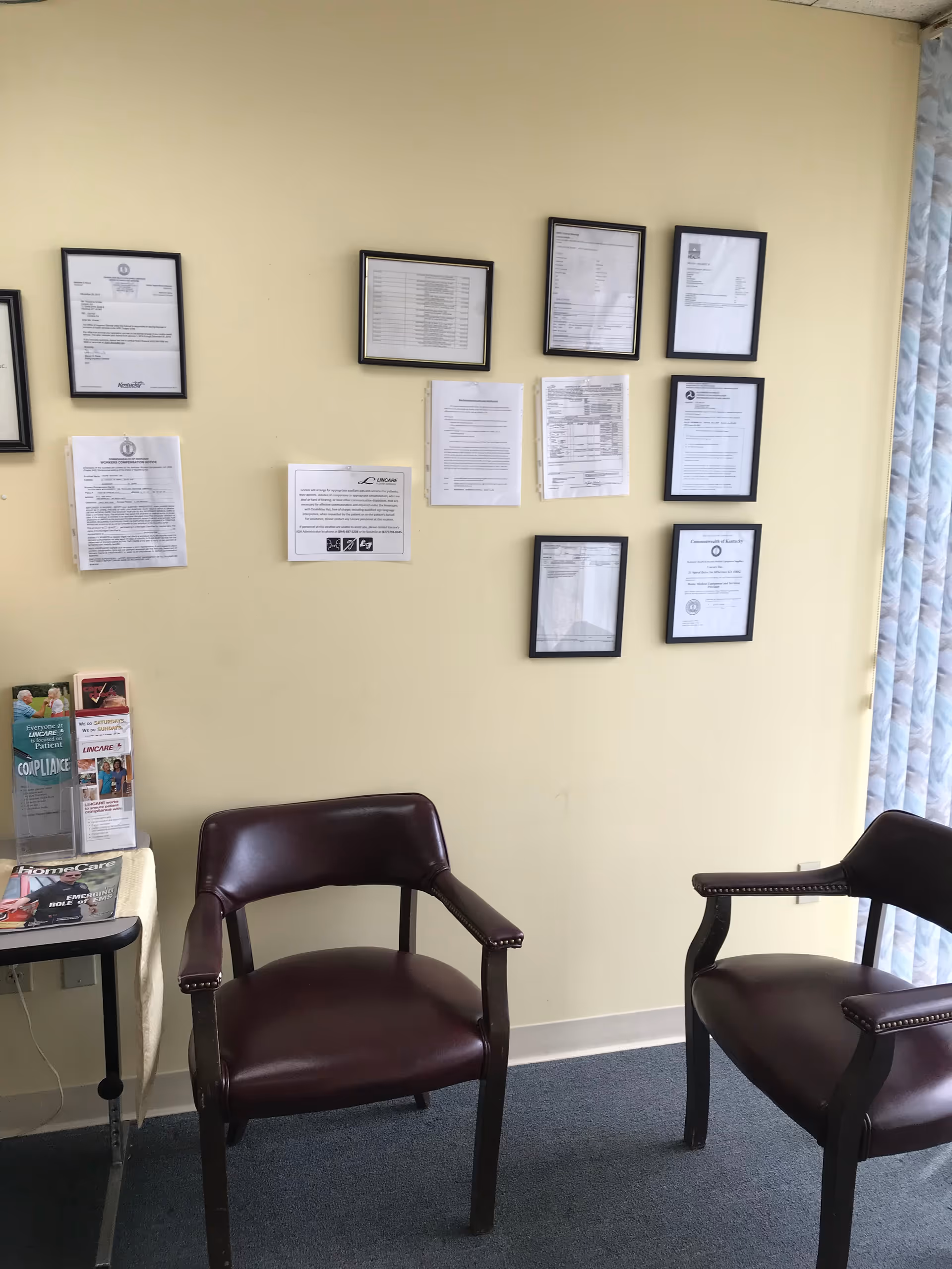 A waiting area with two burgundy chairs, a small table with magazines, and wall notices.