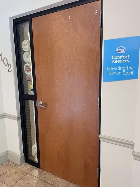 Wooden door with glass panel in a hallway, Comfort Keepers sign mounted on the wall.