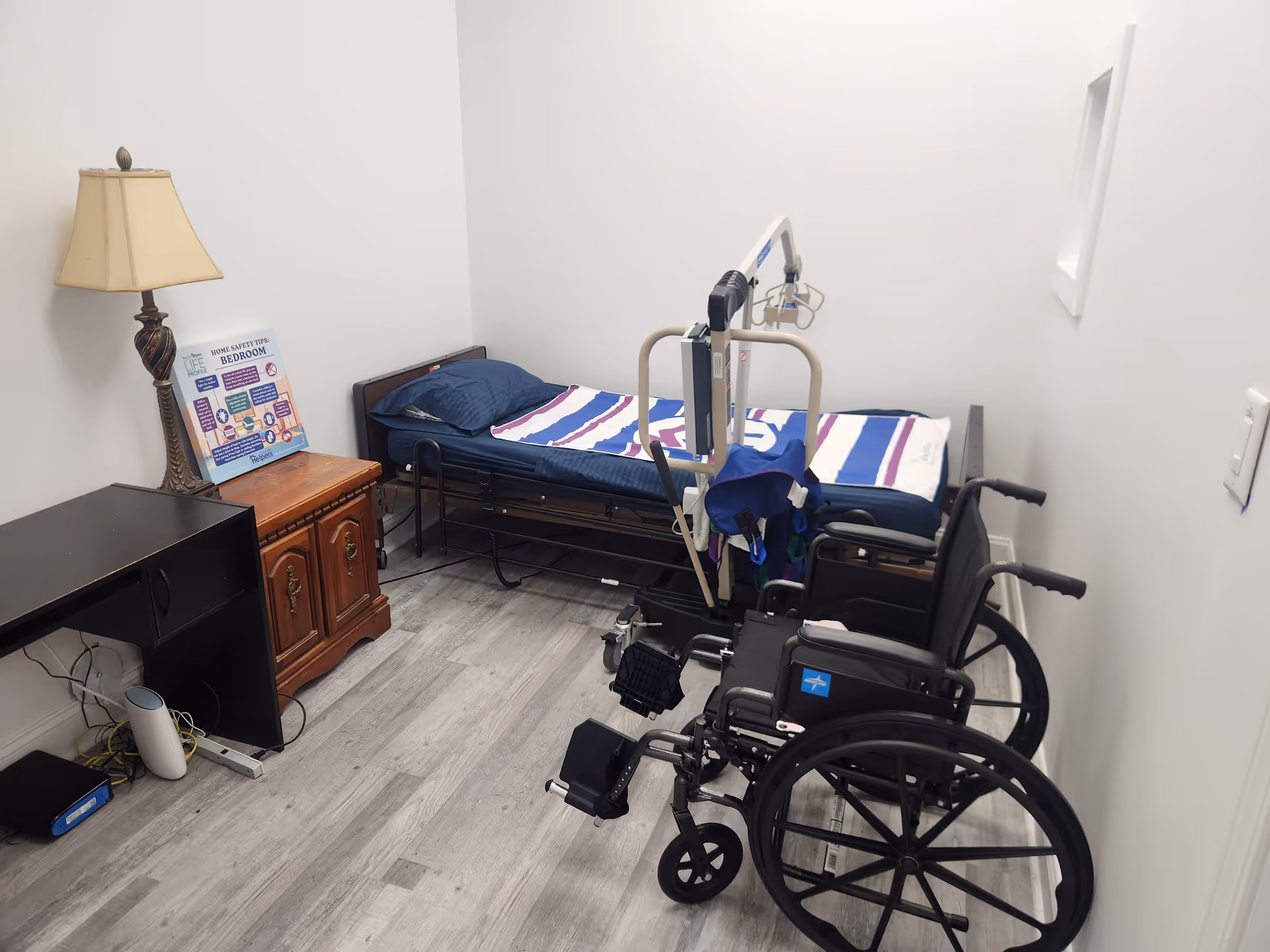 Small bedroom in a senior facility with a single bed, wheelchair, and medical equipment.