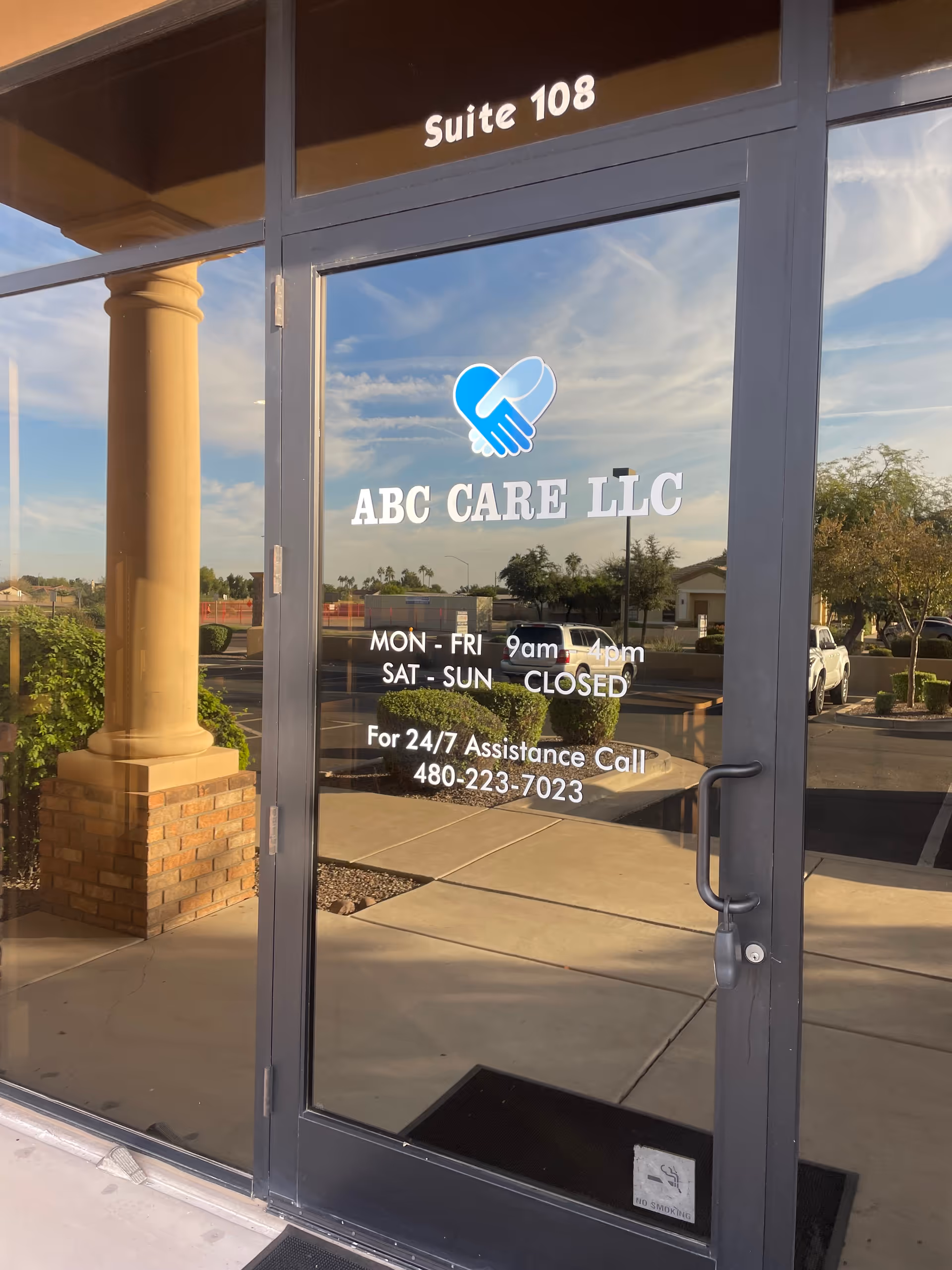 Glass entrance door with ABC CARE LLC sign and reflections of a parking lot.