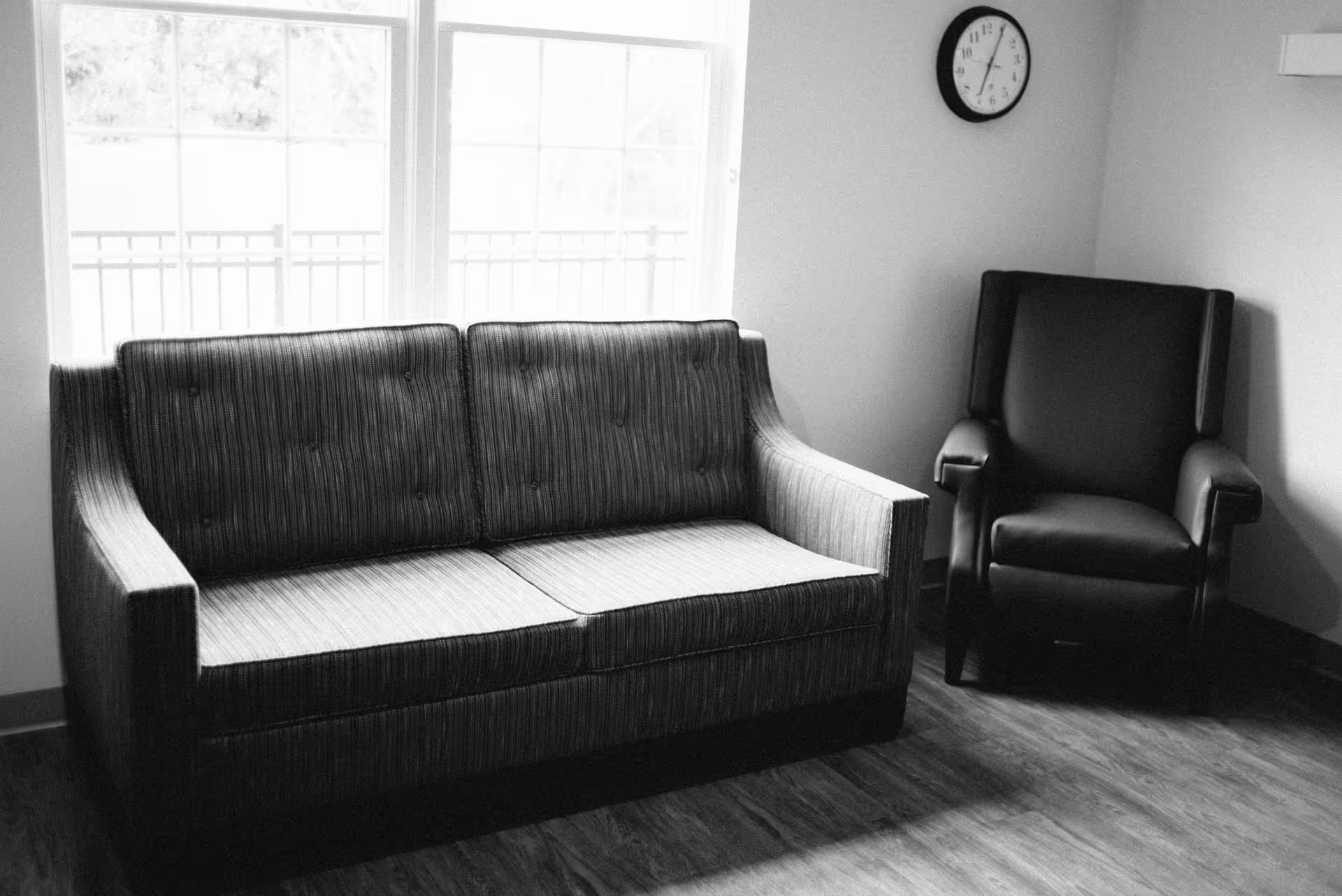 A small lounge area with a sofa, an armchair, and a windowed wall.