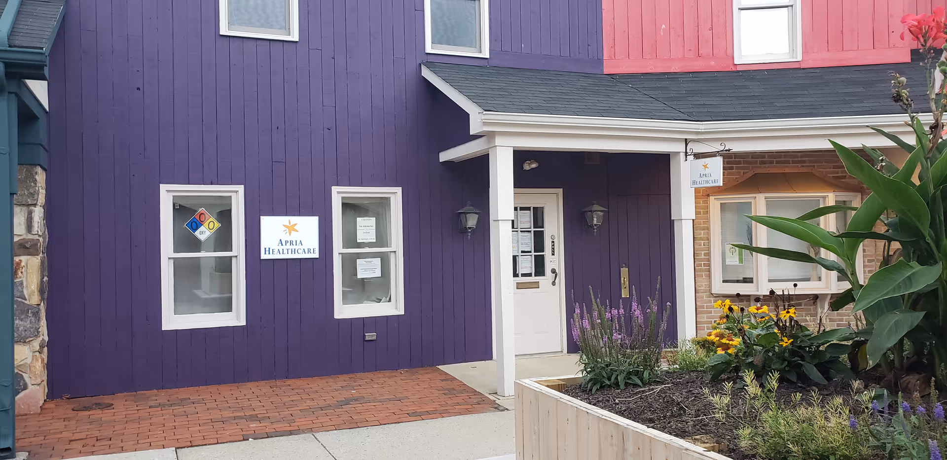 Colorful building exterior with purple siding, white door, and landscaped front.