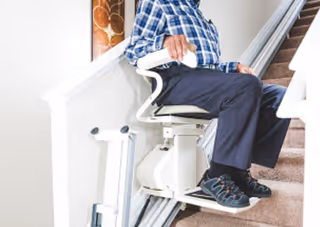 Senior sits on a stairlift chair attached to an indoor staircase.