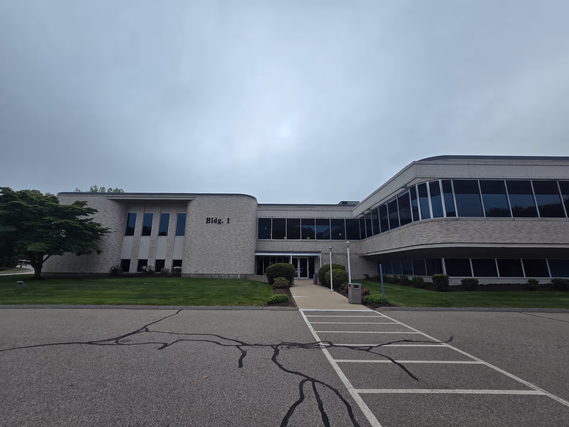 Two-story beige brick building with glass windows and a central entrance, labelled Bldg. 1.
