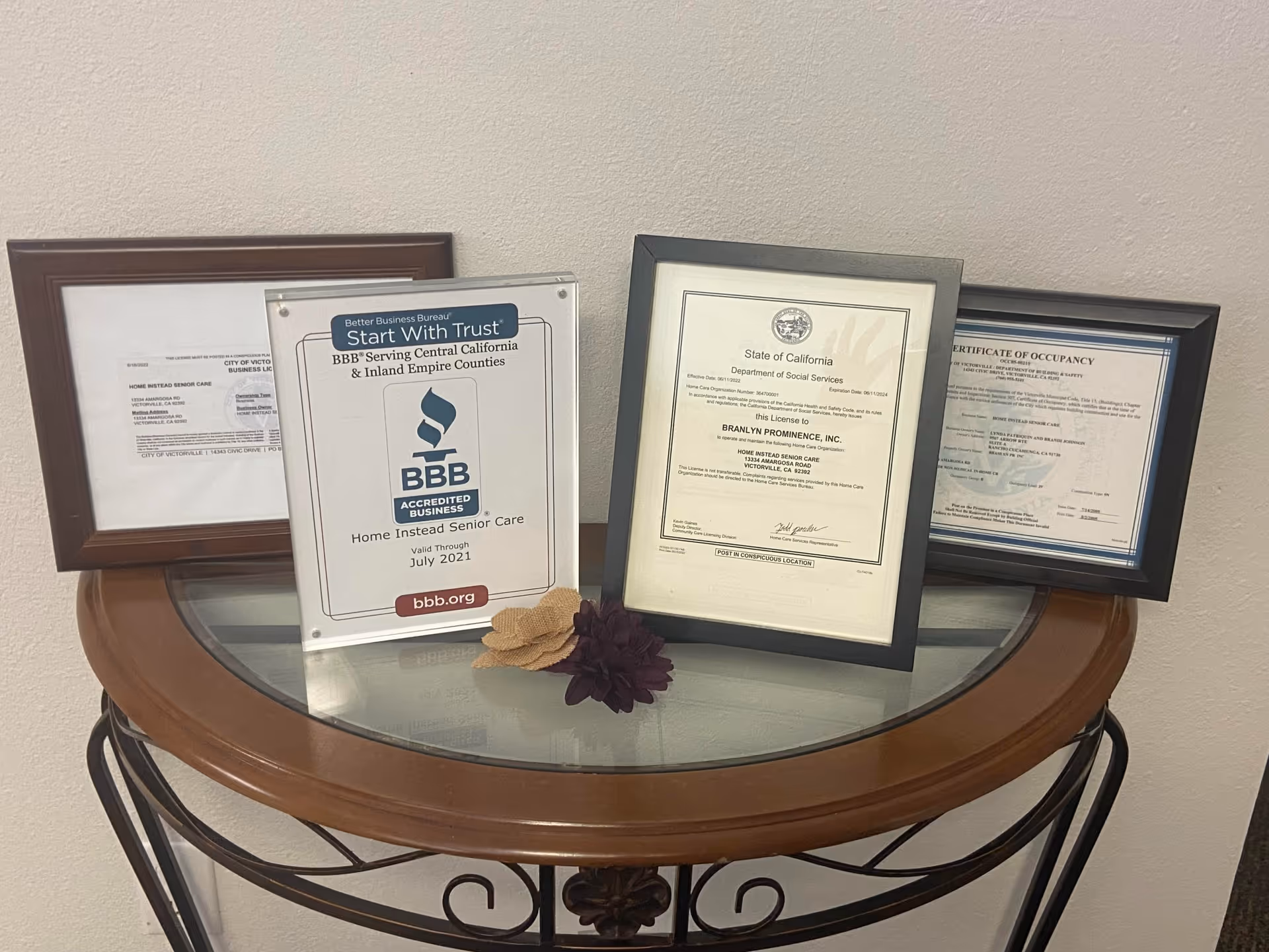 Round glass-top table displays framed certificates against a beige wall.