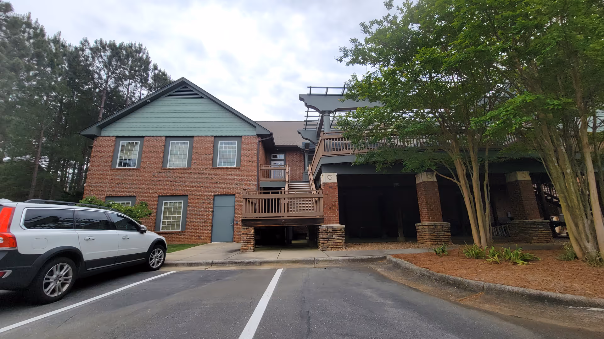 Exterior view of a brick and green-siding senior living facility with stairs and a parked SUV.