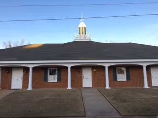 A single-story brick facility with white columns, doors, and a central cupola on the roof.