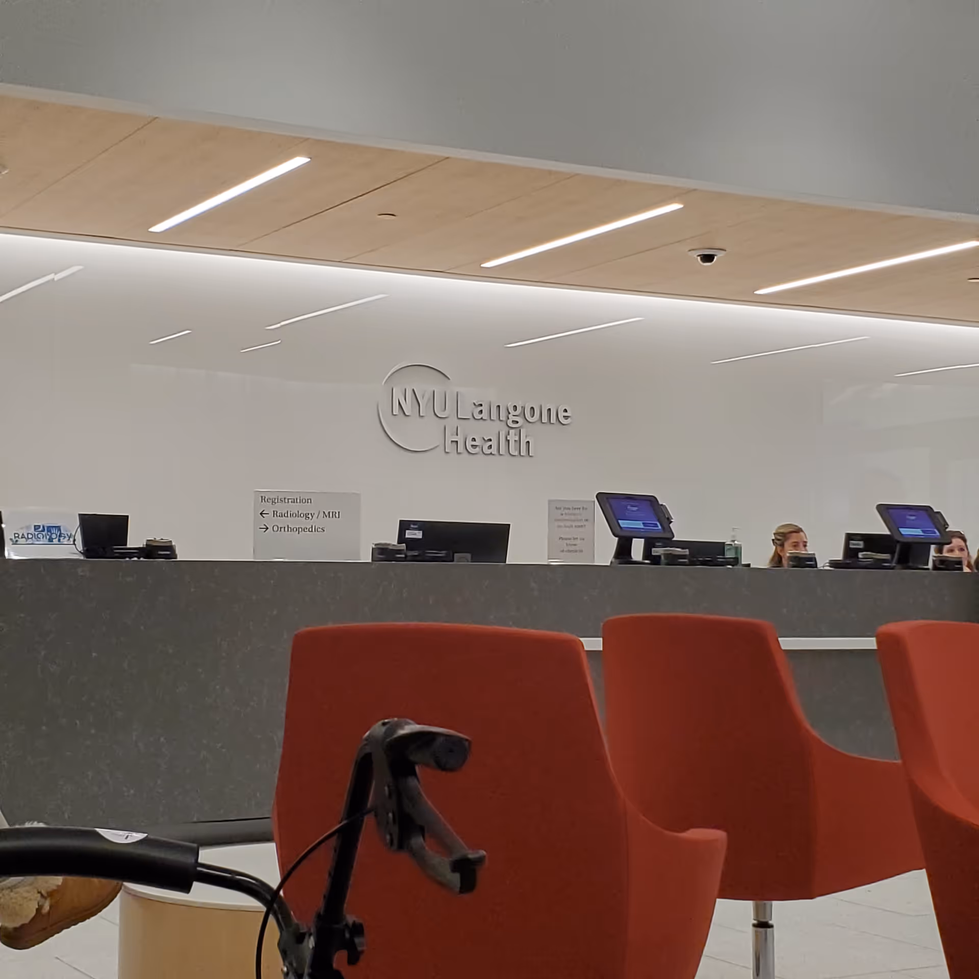 Reception area inside NYU Langone Health with front desk, signage, and red chairs.