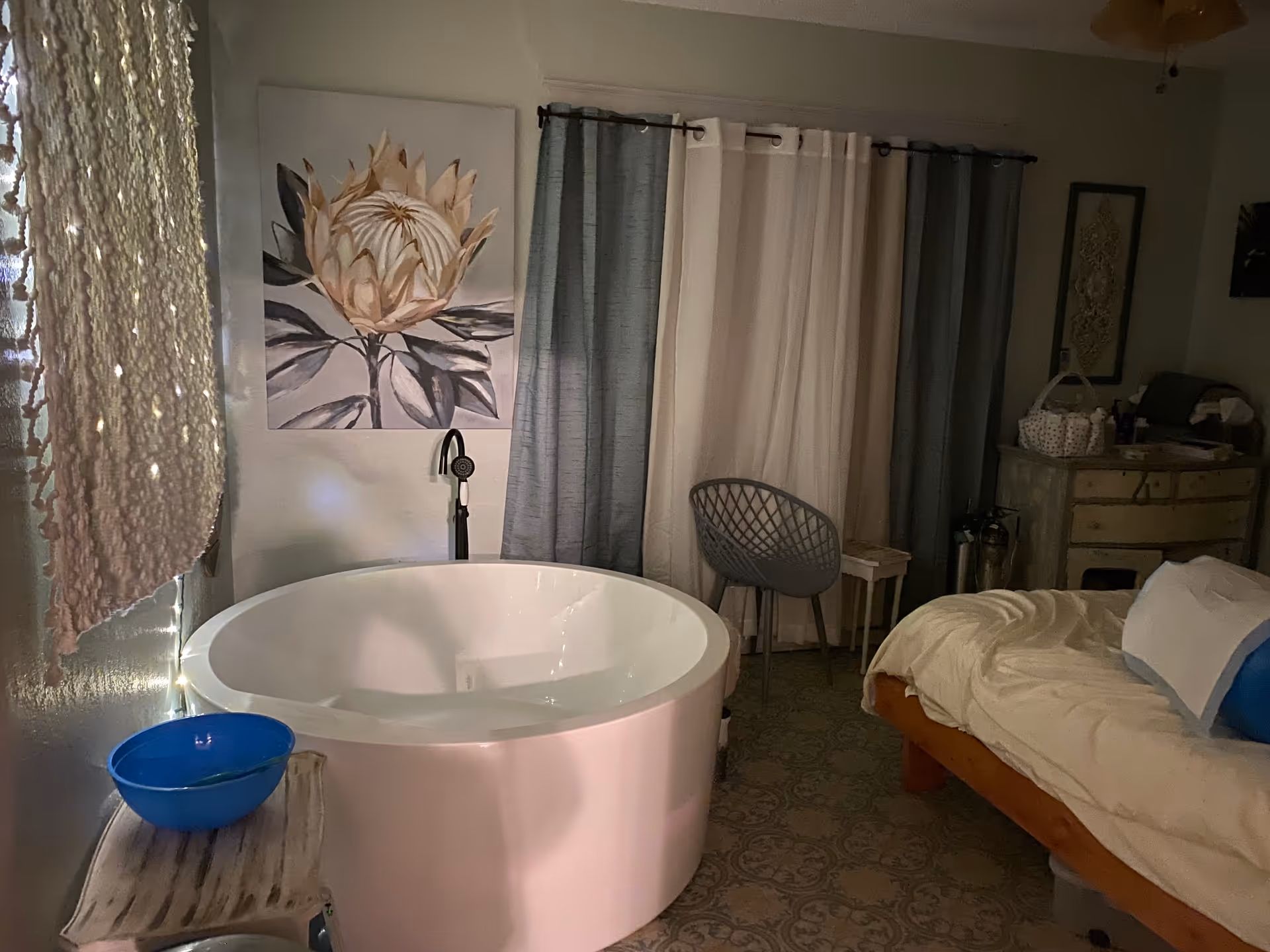 Softly lit birthing room with a round pink tub beside a bed and curtains.