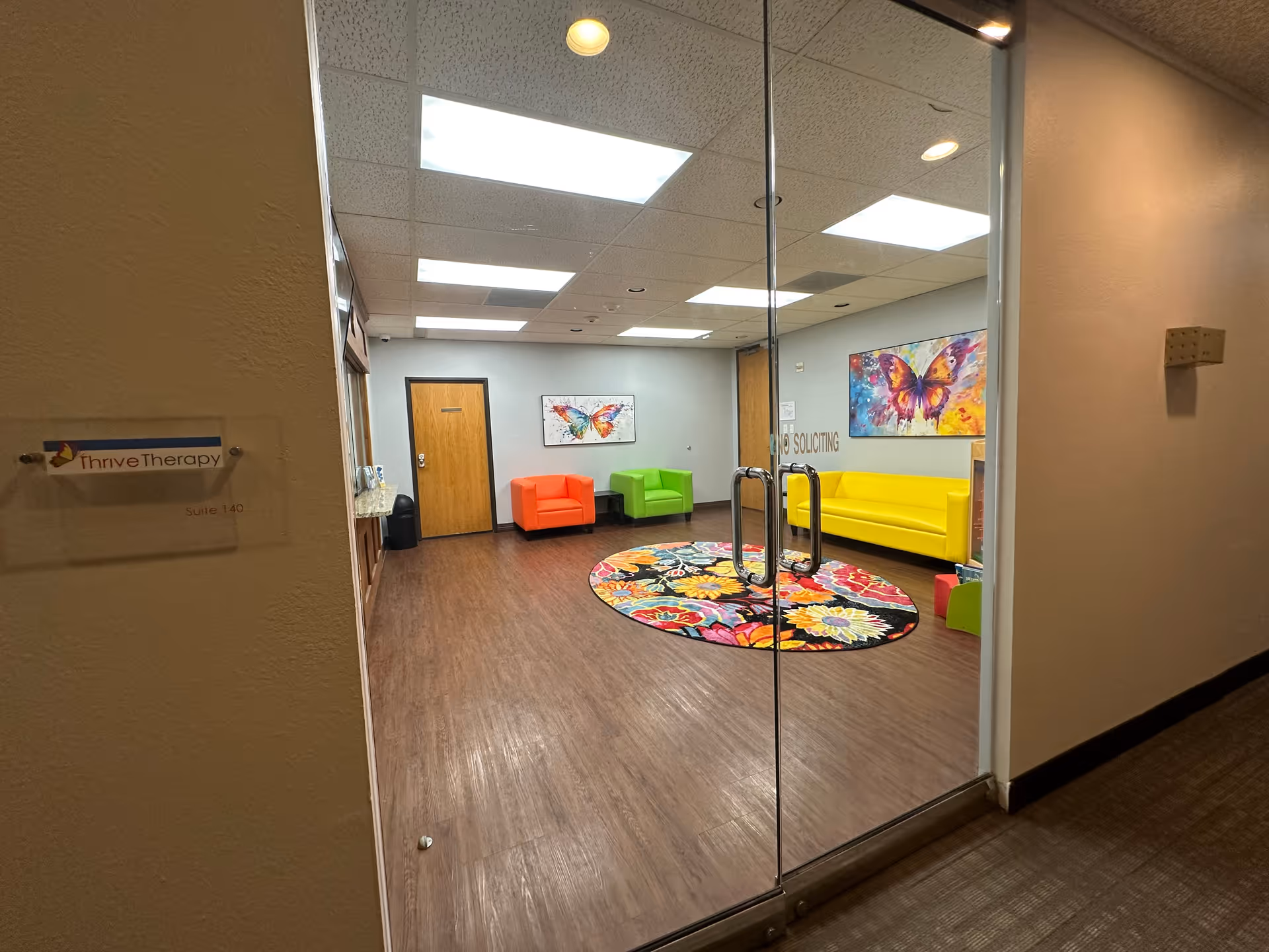 Glass doors open into a colorful lounge with bright chairs, butterfly art, and a circular rug.